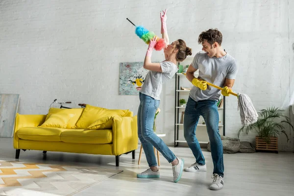 Uomo e donna con la famiglia che cantano mentre fanno le pulizie primaverili in soggiorno — Foto stock