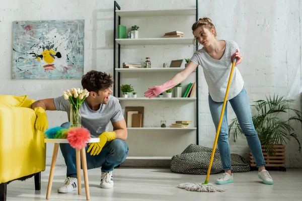 Menina atraente com a mão estendida olhando para o homem limpeza em casa — Fotografia de Stock