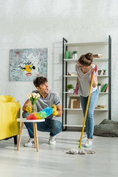 Aufgeregter Mann und glückliche Frau schauen einander beim Putzen im Wohnzimmer an — Stockfoto