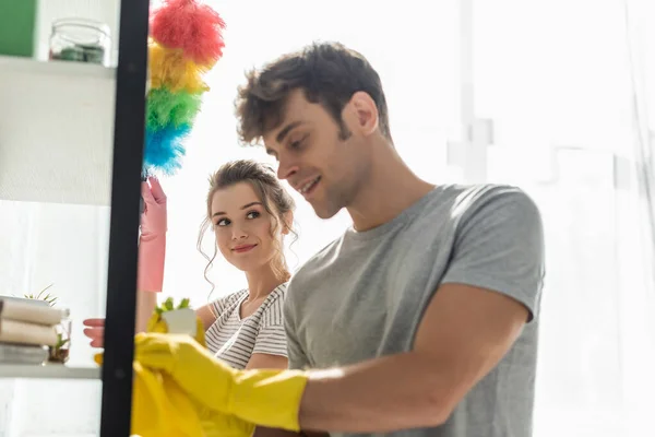 Enfoque selectivo de chica atractiva mirando hombre feliz estante de limpieza en casa - foto de stock