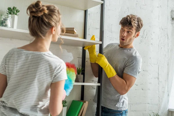 Selective focus of surprised man cleaning rack shelves near girl at home — Stock Photo