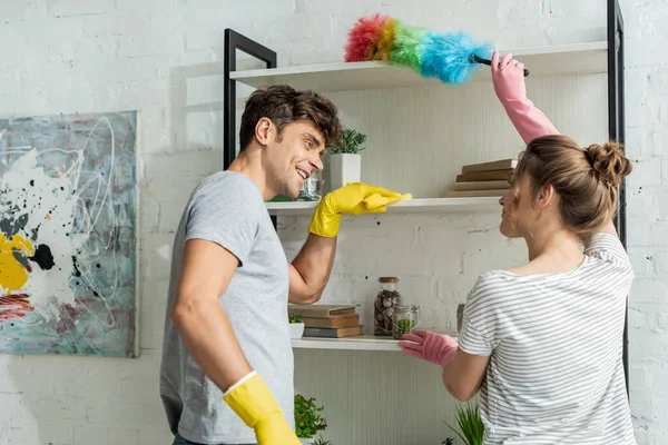 Selective focus of happy girl and man cleaning rack shelves at home — Stock Photo