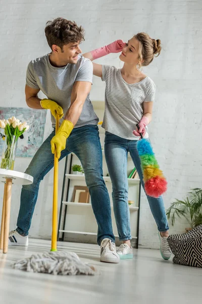 Вибірковий фокус весела дівчина і чоловік, дивлячись один на одного під час прибирання у вітальні — стокове фото