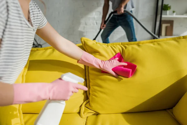 Обрезанный вид девушки стиральной диван с тряпкой рядом мужчина уборка гостиной с пылесосом — стоковое фото