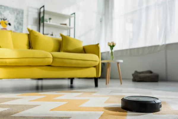 Foco seletivo de robótico aspirador de pó tapete de lavagem perto do sofá na sala de estar — Fotografia de Stock