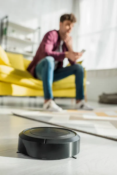 Selective focus of robotic vacuum cleaner washing carpet near man in living room — Stock Photo