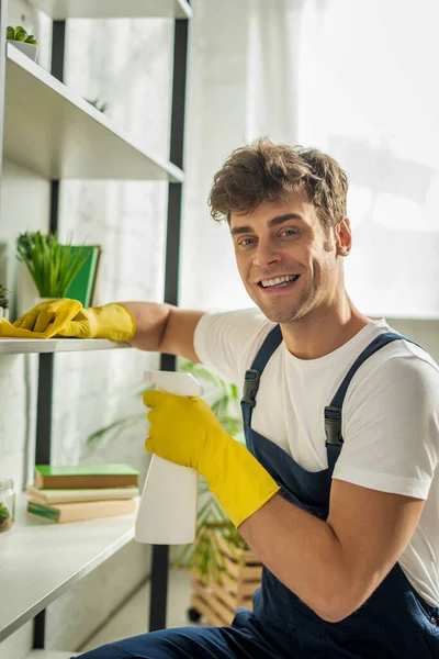Cheerful cleaner in overalls cleaning rack shelves in apartment — Stock Photo