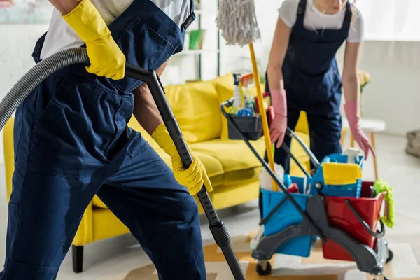 Vista cortada de produtos de limpeza em macacão e luvas de borracha apartamento de limpeza — Fotografia de Stock