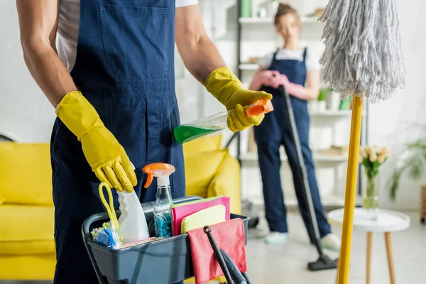 Selective focus of cleaner holding spray bottle near cleaning trolley — Stock Photo