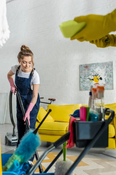 Selective focus of attractive cleaner using vacuum cleaner near coworker with sponge — Stock Photo