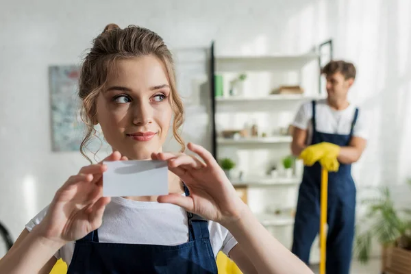 Selective focus of attractive cleaner holding blank card — Stock Photo