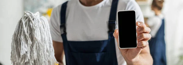 Panoramic shot of cleaner holding smartphone with blank screen and mop — Stock Photo