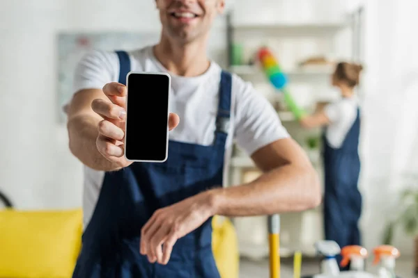 Vista recortada de limpiador feliz celebración de teléfono inteligente con pantalla en blanco - foto de stock