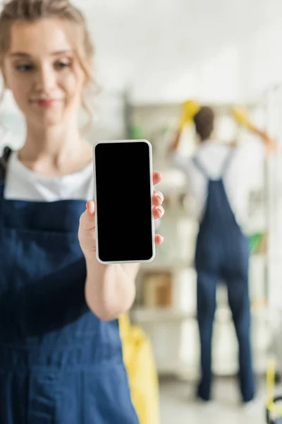 Enfoque selectivo vista de limpiador positivo celebración de teléfono inteligente con pantalla en blanco - foto de stock