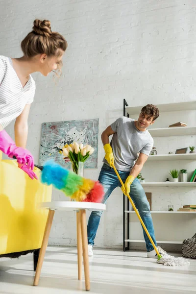 Foco seletivo de homem bonito e mulher jovem fazendo limpeza de primavera no apartamento — Fotografia de Stock