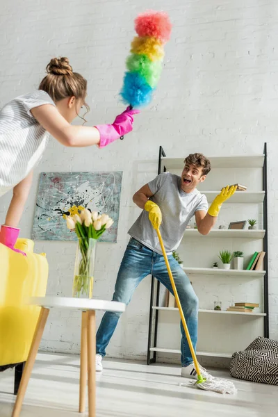 Enfoque selectivo del hombre guapo mirando a la mujer joven haciendo limpieza de primavera en el apartamento - foto de stock