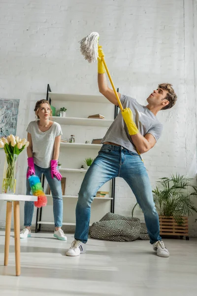 Young and surprised woman looking at handsome man with mop — Stock Photo