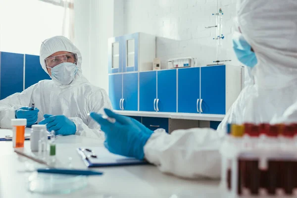 Dos bioquímicos hablando mientras están sentados en el laboratorio cerca de los tubos de ensayo con muestras de sangre - foto de stock