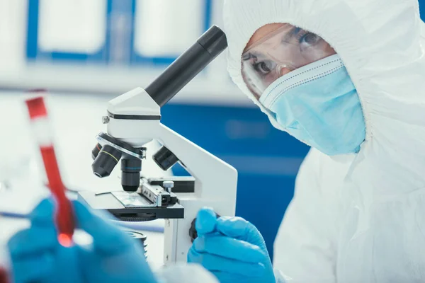 Foyer sélectif du biochimiste près du microscope, en regardant la éprouvette avec échantillon de sang — Photo de stock