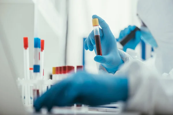 Foco seletivo do bioquímico segurando tubo de teste com amostra de sangue perto colega — Fotografia de Stock