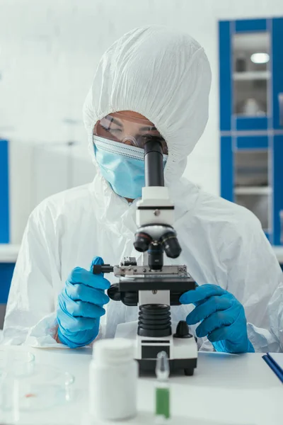 Selective focus of biochemist in hazmat suit looking through microscope — Stock Photo