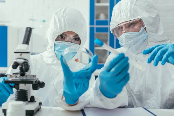 Biochemiker halten Reagenzglas und Petrischale in Mikroskopnähe — Stockfoto