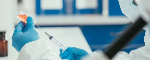 Vista parcial del bioquímico tomando medicamentos del recipiente de vidrio con jeringa, inyección panorámica - foto de stock