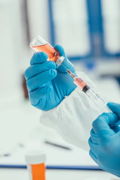 Cropped view of biochemist taking medicine from glass container with syringe — Stock Photo