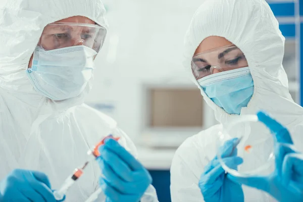 Біохімік, який приймає ліки зі шприцом біля колеги, що тримає страву Петрі — стокове фото