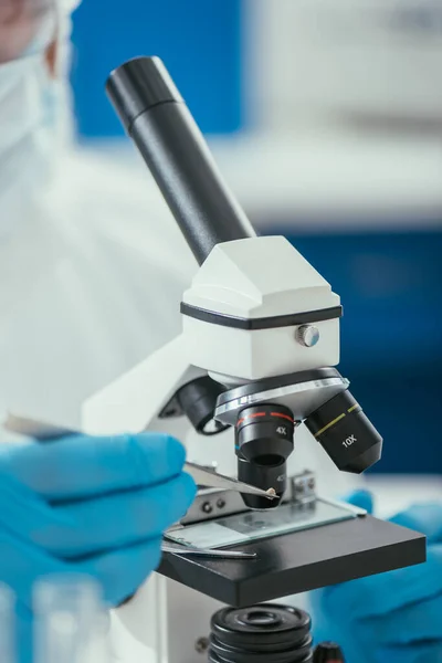 Partial view of biochemist looking through microscope at small stone — Stock Photo