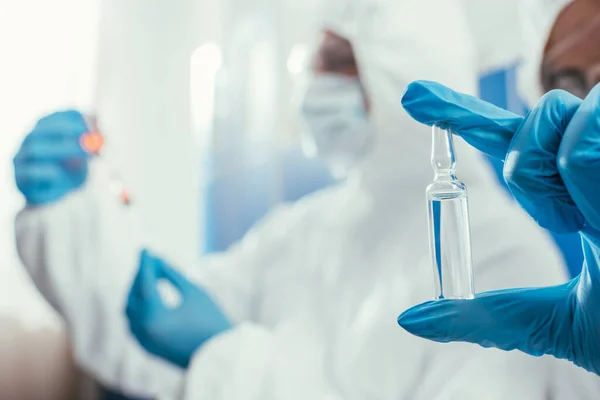 Foco seletivo do bioquímico segurando ampola com a medicina perto colega — Fotografia de Stock