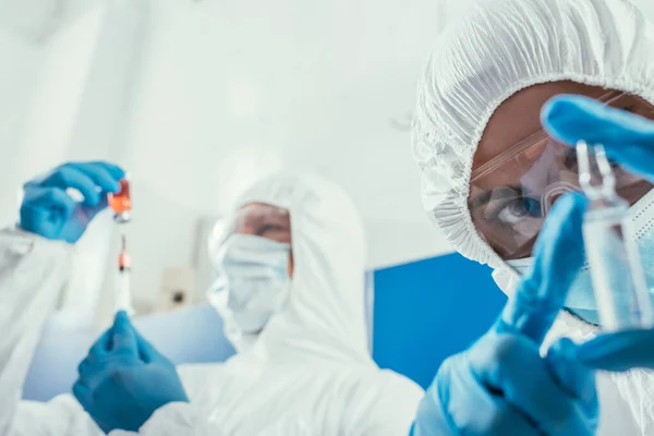 Foyer sélectif du biochimiste regardant ampule près de son collègue prenant un médicament avec une seringue — Photo de stock