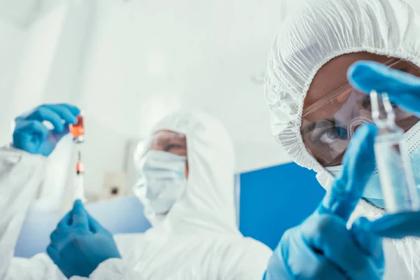 Foco seletivo do bioquímico olhando para ampola perto colega tomar medicamento com seringa — Fotografia de Stock