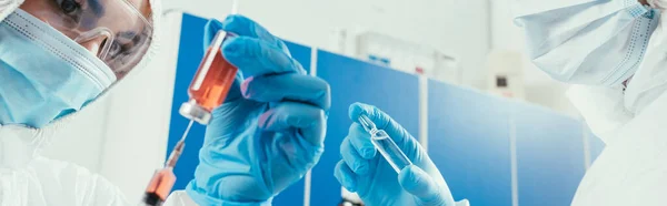 Panoramic shot of biochemist taking medicine with syringe near colleague holding ampule — Stock Photo