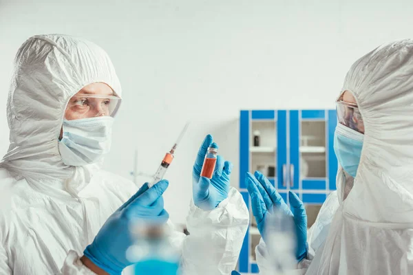 Bioquímico que sostiene la jeringa y el envase con la medicina cerca de colega en laboratorio - foto de stock