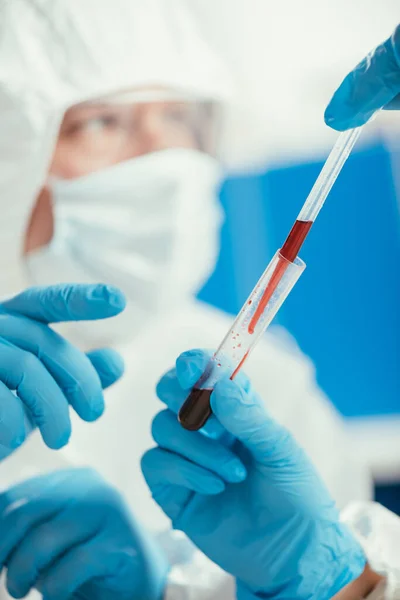 Visão cortada de bioquímico segurando pipeta e tubo de ensaio com amostra de sangue perto colega — Fotografia de Stock