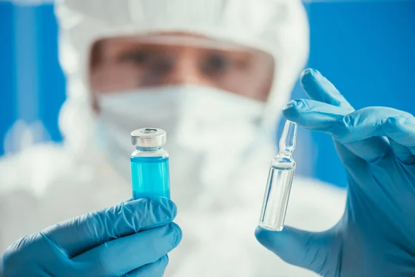 Enfoque selectivo del bioquímico sosteniendo ampollas y envases de vidrio con medicamentos - foto de stock