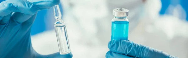 Partial view of biochemist holding glass container with blue liquid and ampule — Stock Photo