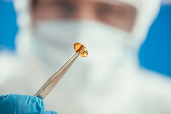 Partial view of biochemist holding capsule with tweezers — Stock Photo