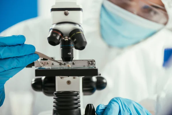 Enfoque selectivo del bioquímico poner piedras pequeñas en el microscopio con pinzas - foto de stock