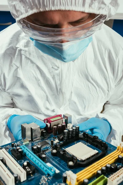 Engineer in hazmat suit, medical mask and goggles holding motherboard — Stock Photo