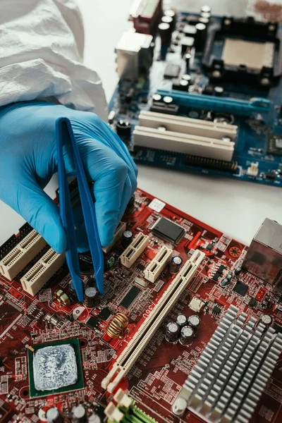 Ausgeschnittene Ansicht des Ingenieurs, der Computermotherboard mit Pinzette befestigt — Stockfoto
