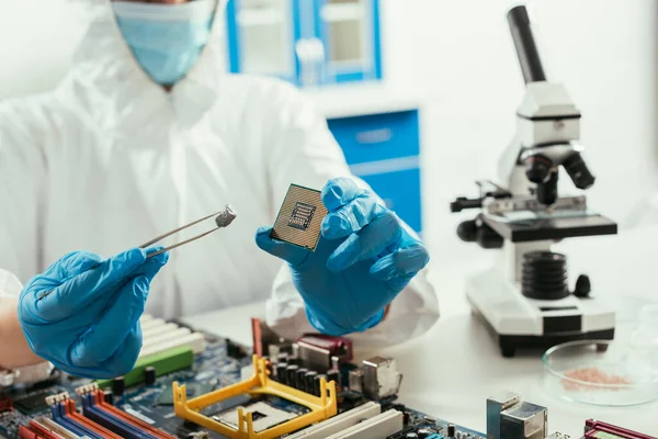 Cropped view of engineer holding microchip and small stone near microscope and computer motherboard — Stock Photo