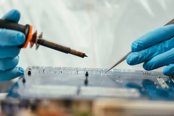 Vista parcial del ingeniero que sostiene el soldador y las pinzas cerca de la placa base de la computadora - foto de stock