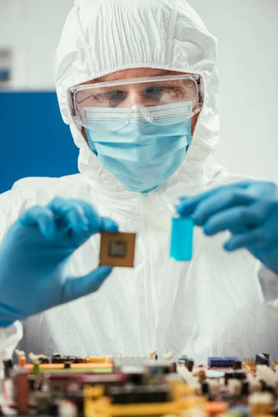 Foco selectivo del ingeniero que sostiene el microchip y el envase de cristal con el líquido azul cerca de la placa madre de la computadora - foto de stock