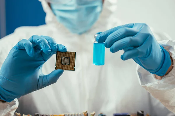 Recortado del ingeniero que sostiene el microchip de la computadora y el envase de cristal con líquido azul - foto de stock