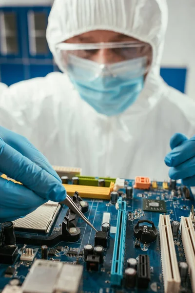 Selective focus of engineer holding tweezers while testing computer motherboard — Stock Photo