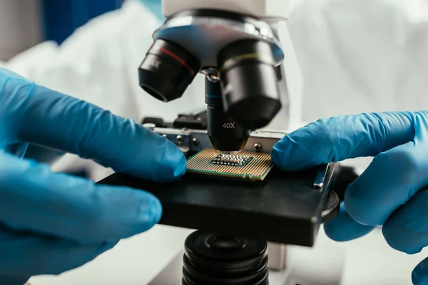 Cropped view of engineer looking at computer microchip through microscope — Stock Photo