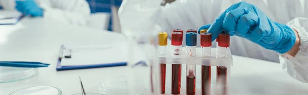 Vista recortada del bioquímico que toma el tubo de ensayo con la muestra de sangre, tiro panorámico - foto de stock