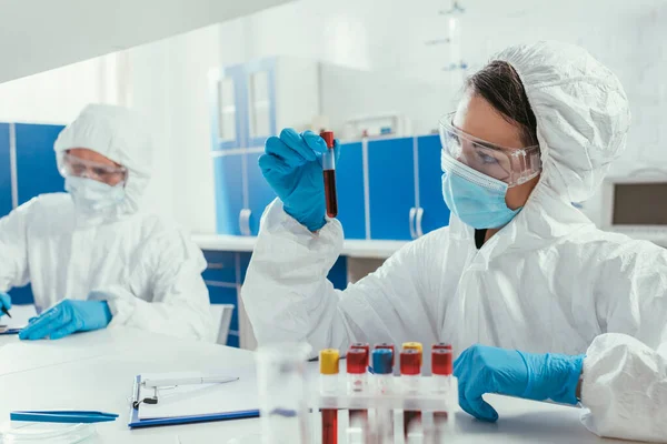 Bioquímico que sostiene el tubo de ensayo con la muestra de sangre cerca de colega en laboratorio - foto de stock